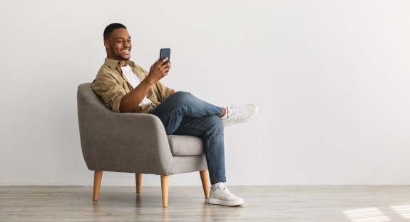 junger Mann sitzt auf einem Stuhl mit Handy in der Hand